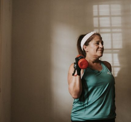 Middle-aged woman in workout attire lifting a dumbbell indoors, promoting fitness and healthy lifestyle.