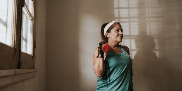 Middle-aged woman in workout attire lifting a dumbbell indoors, promoting fitness and healthy lifestyle.