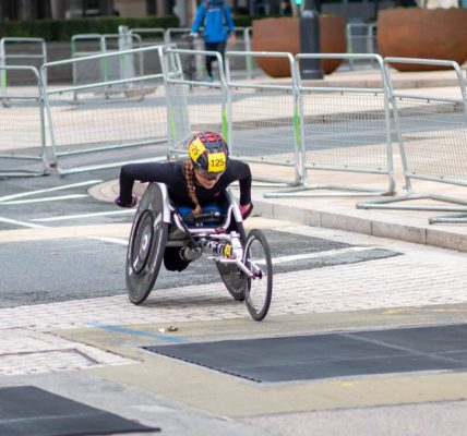 A dedicated athlete competes in a marathon using a racing wheelchair on city streets.